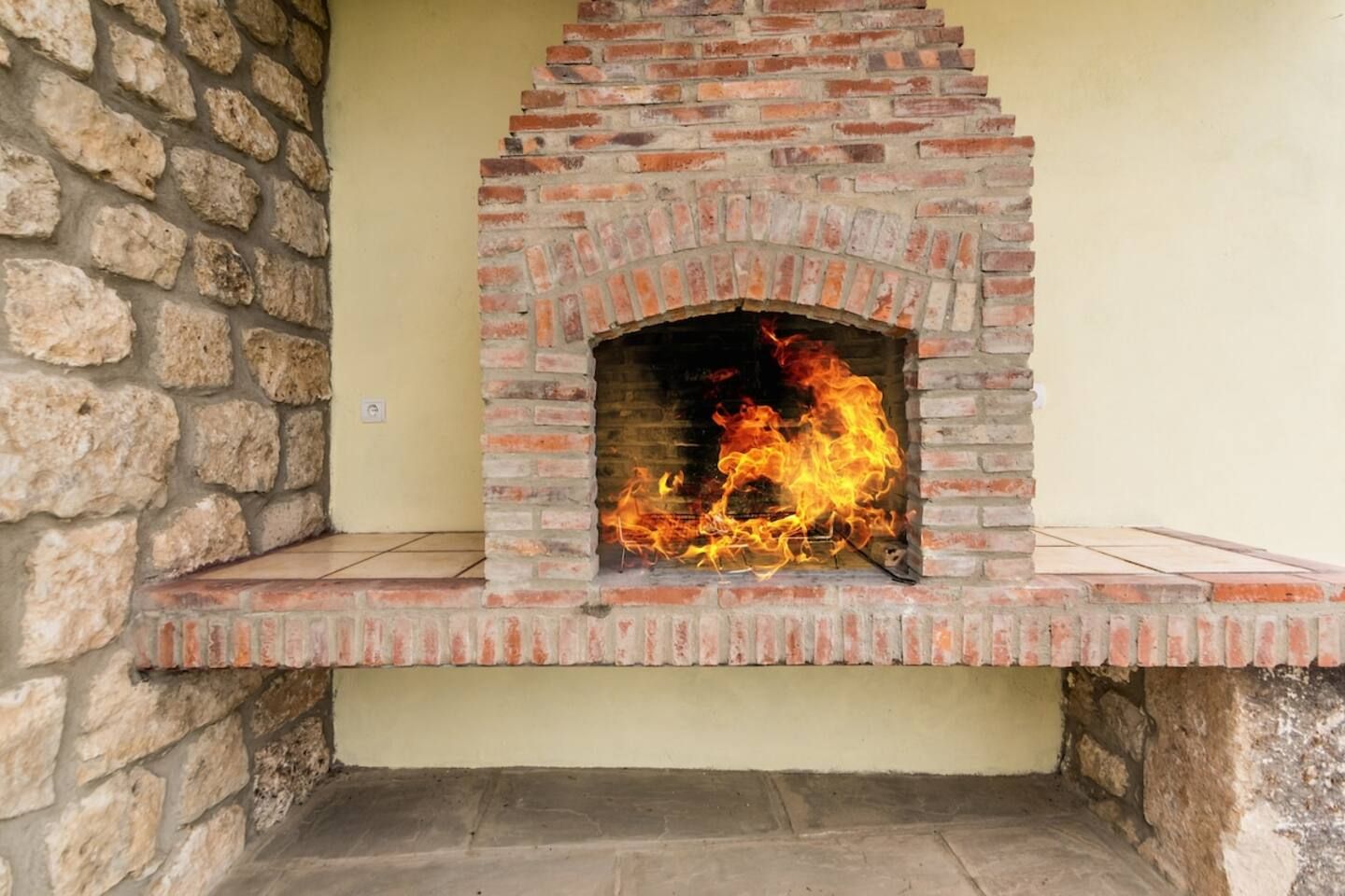 A brick-built outdoor fireplace with a fire burning inside.