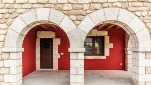 A stone building with two arched doorways and a red wall. - Fidalsa Rest Station (Villadiego)