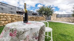 A table with a floral tablecloth, two wine glasses, and a bottle of wine, set outdoors with a stone wall and a tree in the background. - Fidalsa Rest Station (Villadiego)