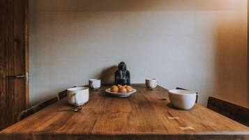 Una mesa de madera con cuatro tazas blancas, un plato de croissants y una cafetera negra.