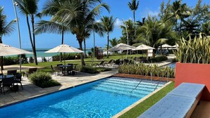 Une piscine entourée de chaises longues et de parasols, bord ée de palmiers et offrant une vue sur l’océan.