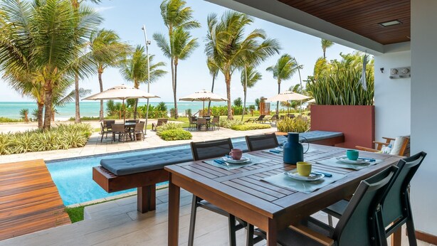 Un espace aménagé au bord de la piscine, avec une table et des chaises en bois, une petite piscine et des palmiers.