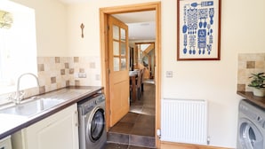 A kitchen with a washing machine, a sink, and a dining area in the background. - Tyn Y Ceubren Bach at Evelyns Retreat (Corwen)
