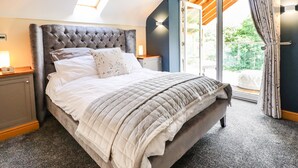 A bedroom with a tufted headboard, a large bed with a quilted duvet, a nightstand with a lamp, and a sliding glass door leading to an outdoor area. - Tyn Y Ceubren Bach at Evelyns Retreat (Corwen)