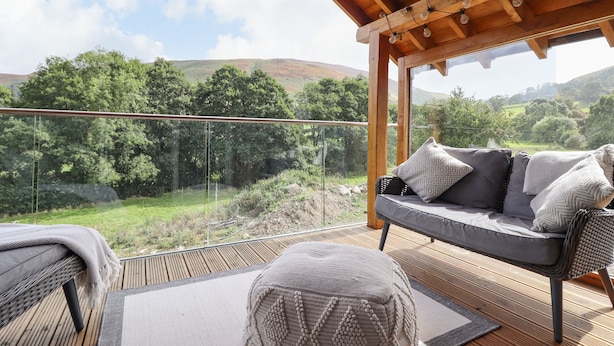 A wooden deck with a sofa and ottoman, overlooking a lush landscape. - Tyn Y Ceubren Bach at Evelyns Retreat (Corwen)