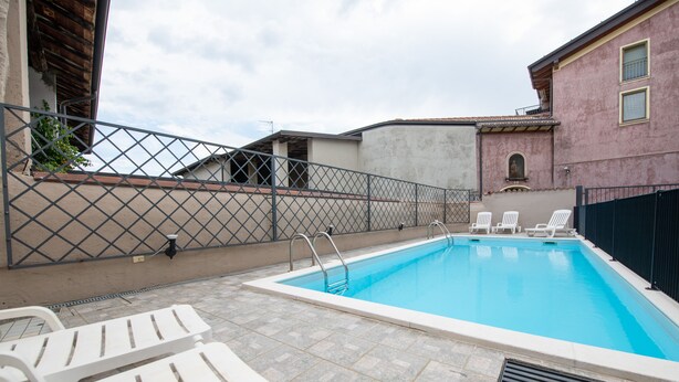 Une piscine dotée d’une terrasse carrelée, entourée d’une clôture en métal et de chaises longues blanches.