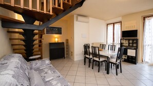 Un salon comprenant un canapé, une table à manger, des chaises, un escalier et un téléviseur.