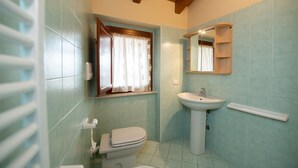 Une salle de bain avec des toilettes, un lavabo et une fenêtre avec des rideaux.