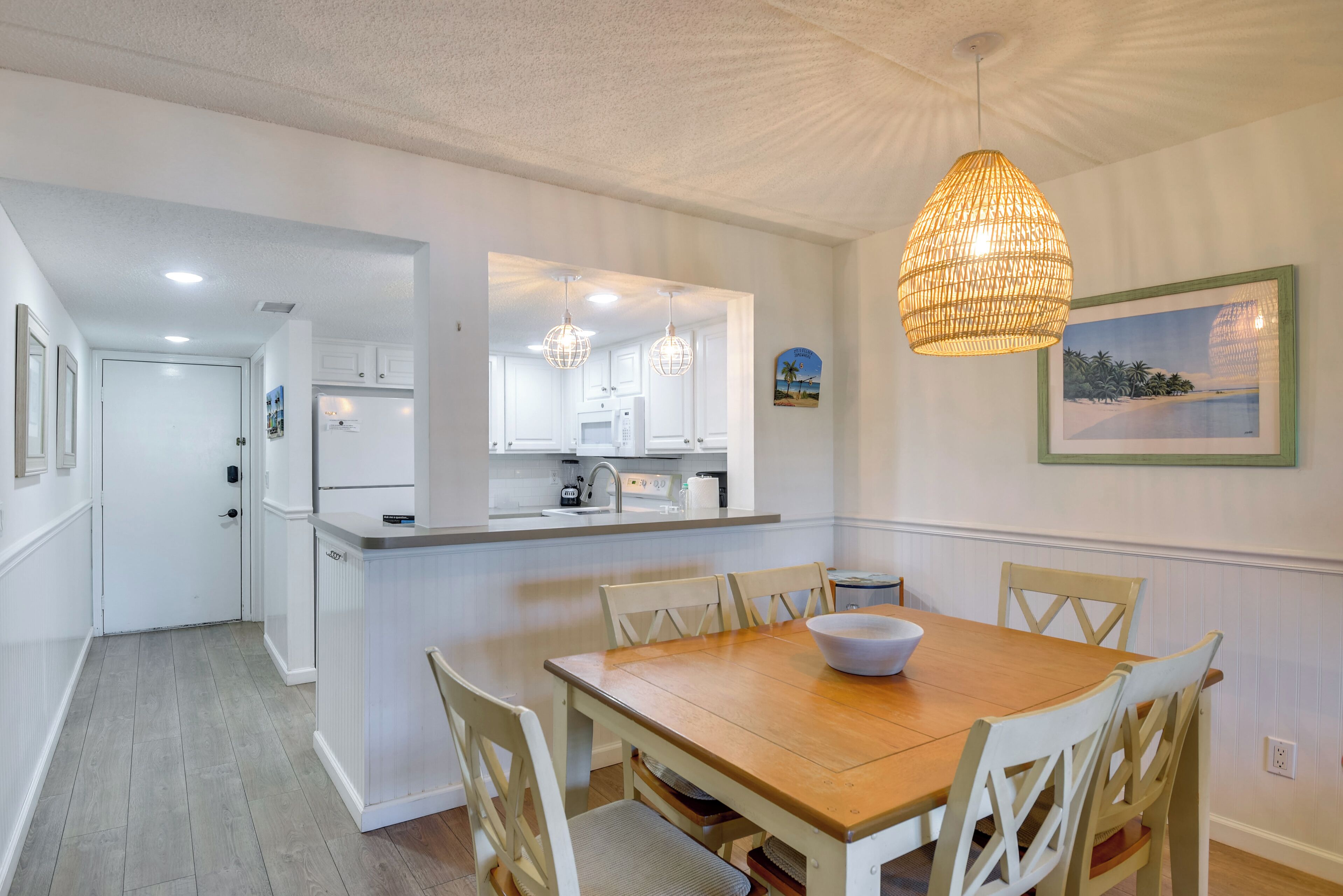 Zona pranzo con tavolo e sedie in legno, cucina con mobili bianchi e lampadario.