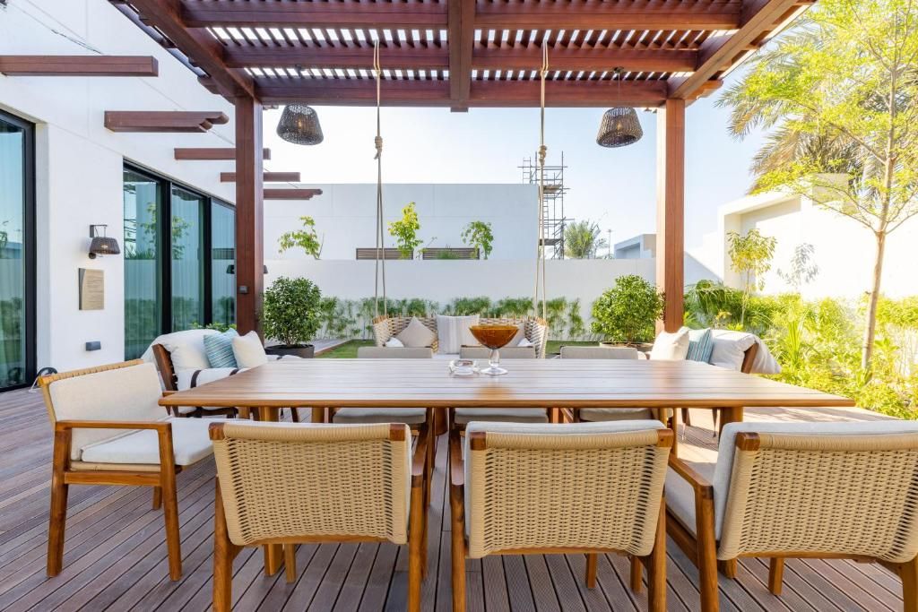Un patio al aire libre con una mesa de madera y sillas de mimbre, rodeado de follaje y un edificio moderno al fondo.