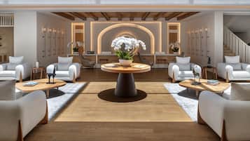 Un vestíbulo de hotel con una mesa redonda central, disposición de asientos y mostrador de recepción.