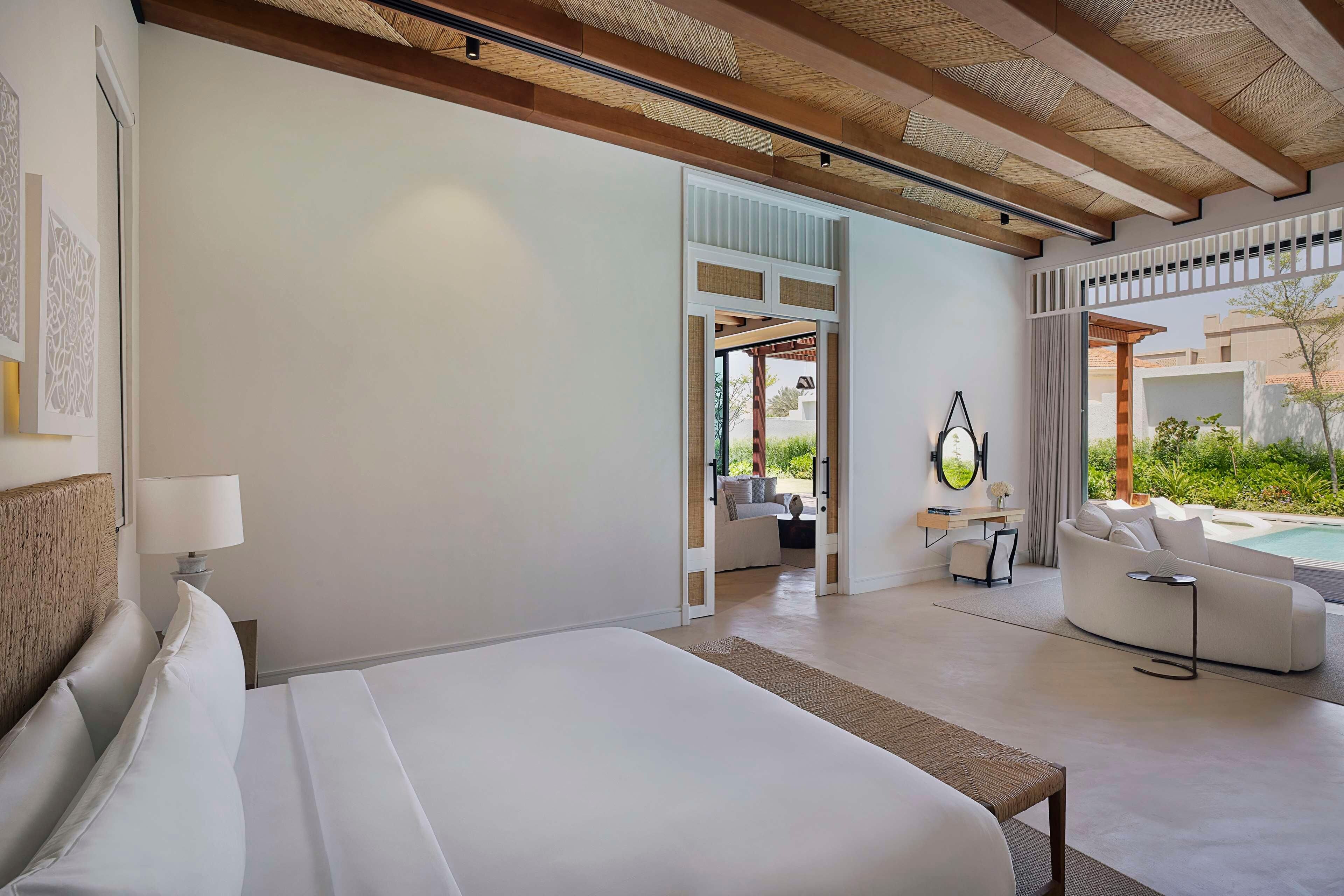 A modern hotel room with a large bed, a sofa, a small table, and a view of the outdoors.