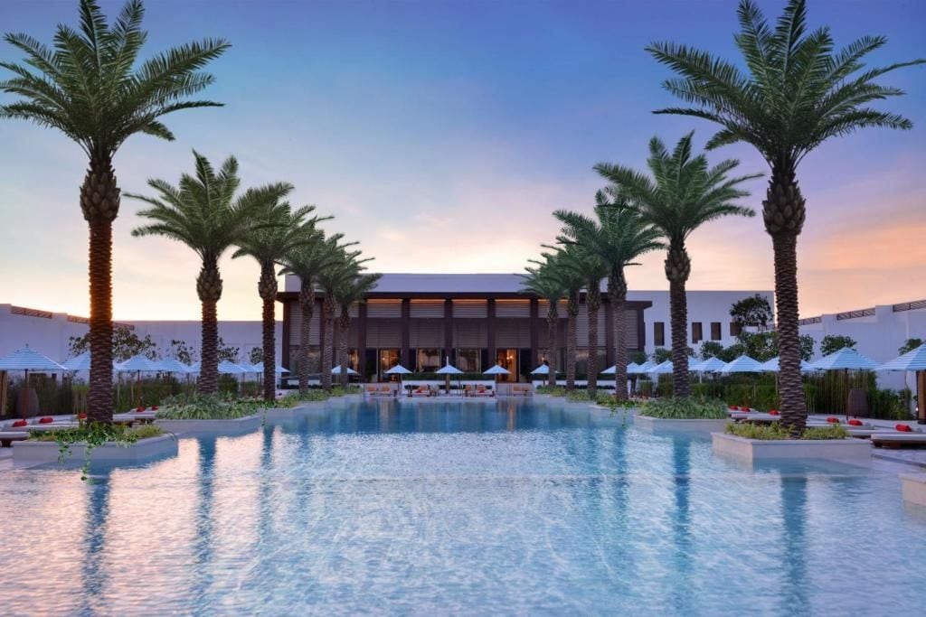 Un hotel con piscina, palmeras y zonas de descanso.