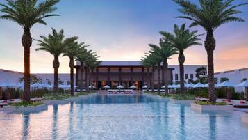 Un hotel con piscina, palmeras y zonas de descanso.