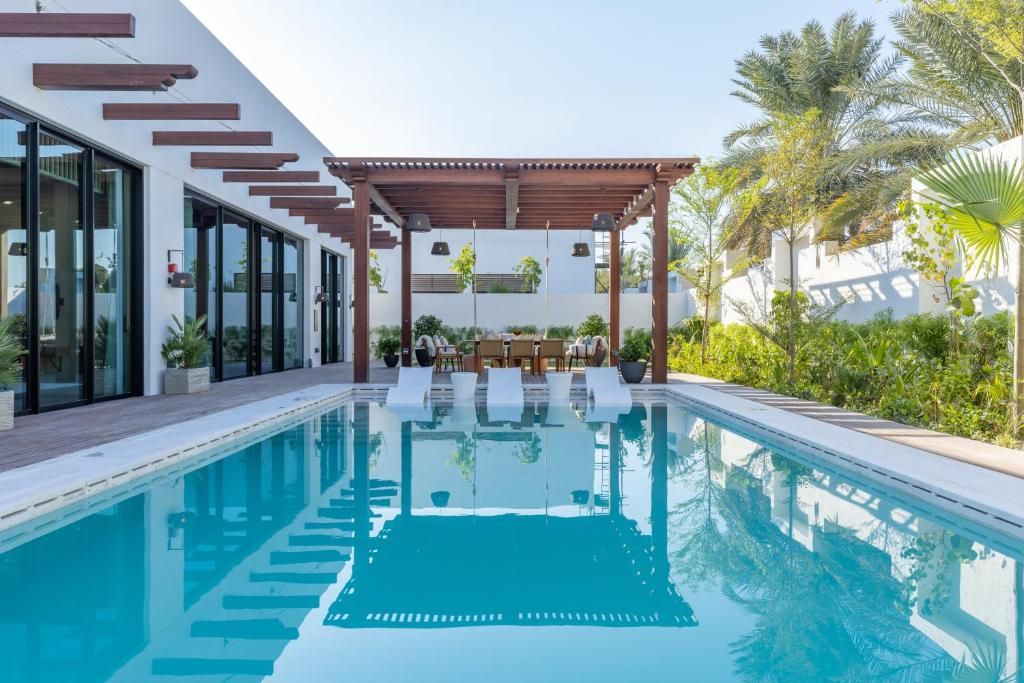 A modern pool area with a clear pool, lounge chairs, and a pergola.