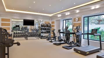 A well-equipped gym with various exercise machines, free weights, and a large window offering a view of greenery.