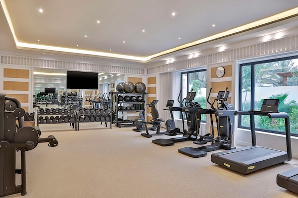 Ein gut ausgestattetes Fitnessstudio mit verschiedenen Trainingsgeräten, Kurzhanteln und einem großen Fenster mit Blick auf Grünflächen.