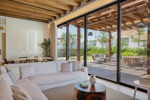 A modern living room with a large white sofa, a round wooden coffee table, and a view of an outdoor deck with furniture. - Maysan Doha Lxr Hotels & Resorts (Al Rayyan)