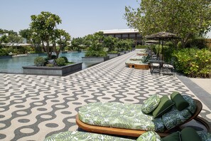 A poolside area with lounge chairs, a patterned floor, and a building in the background. - Maysan Doha Lxr Hotels & Resorts (Al Rayyan)