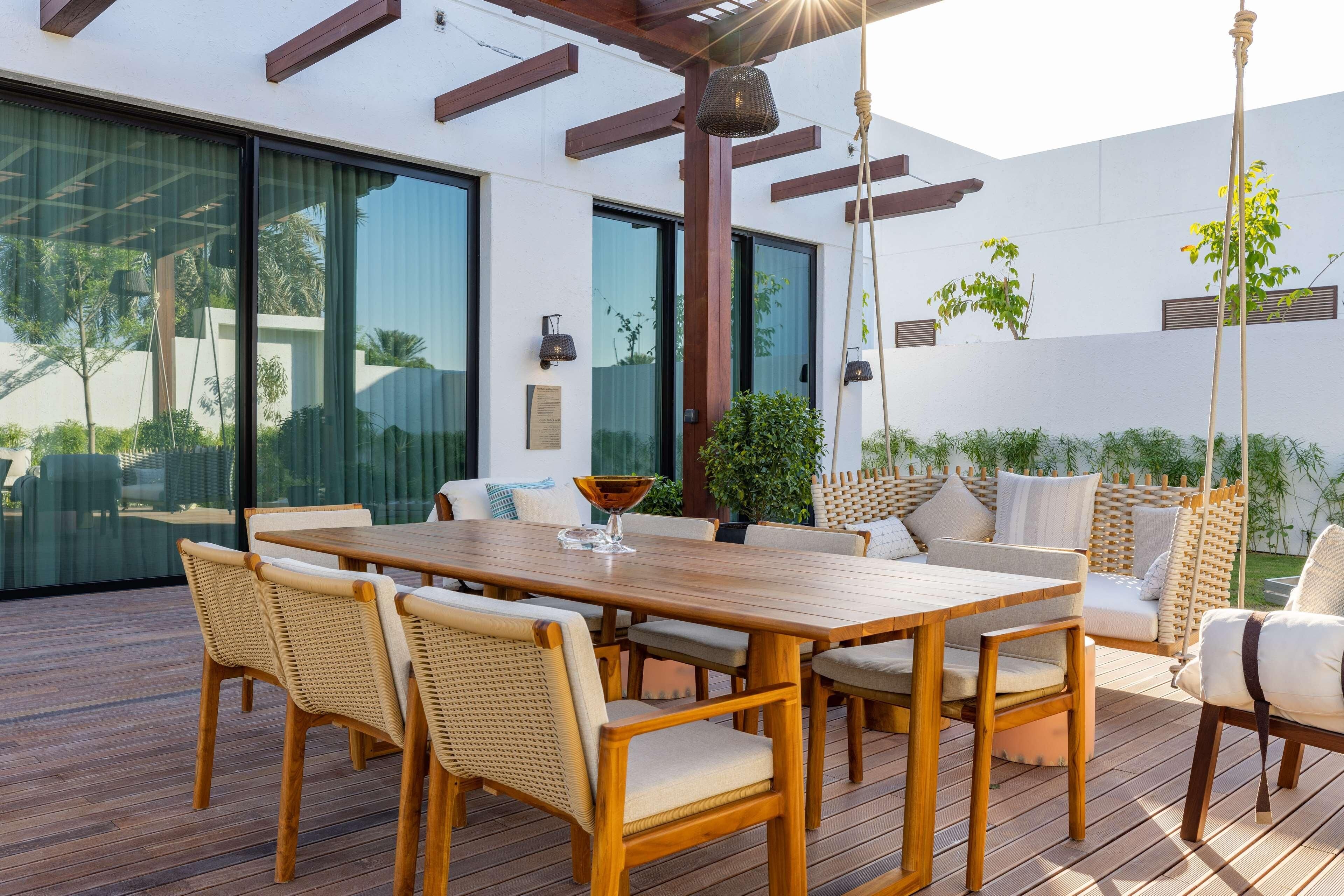 Un patio al aire libre con una mesa y sillas de madera, rodeado por un muro blanco y puertas de cristal.