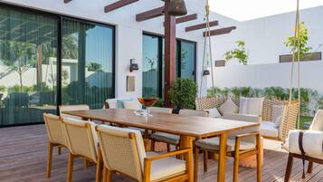 Un patio al aire libre con una mesa y sillas de madera, rodeado por un muro blanco y puertas de cristal.