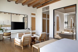 A modern bedroom with a large bed, two chairs, a desk, and a bathroom with a bathtub. - Maysan Doha Lxr Hotels & Resorts (Al Rayyan)