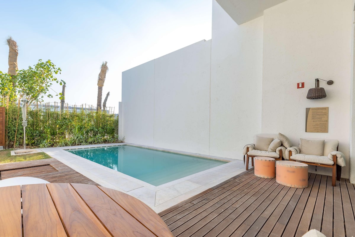 A modern outdoor pool area with a wooden deck, a lounge chair, and a table.