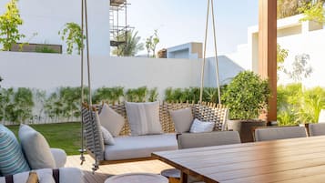Un espacio al aire libre con mesa de madera, asientos acolchados y una silla colgante.