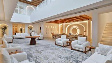 Ambiente spazioso e luminoso, con soffitto alto, diverse zone relax e un tavolino da caffè al centro.