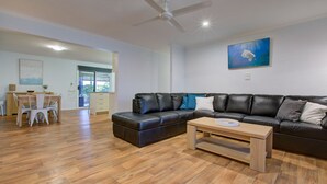 Un salon moderne avec un canapé d’angle en cuir noir, une table basse en bois et un coin repas comprenant une table et des chaises en bois.