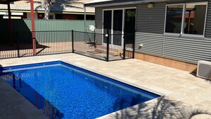 Une piscine avec une terrasse carrelée, un patio délimité par une clôture et un bâtiment à la façade métallique.