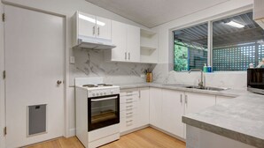 A modern kitchen with white cabinets, a stove, oven, and a large window with a view of greenery.