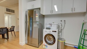 A compact kitchen with a stainless steel refrigerator, a Bosch washing machine, and white cabinets.