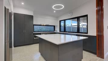 Une cuisine moderne dotée d’un grand îlot central, de meubles de rangement aux couleurs sombres et offrant une vue sur l’extérieur grâce à une fenêtre.