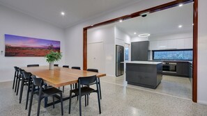 A modern kitchen with a central island, a dining area with a wooden table and chairs, and a large painting on the wall. - Amberjack is an outdoor lovers delight. (Exmouth)