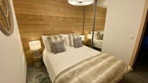 Un dormitorio con cabecera de madera, cama con ropa blanca y varias almohadas, lámparas de noche, una alfombra mullida y un espejo en la pared.