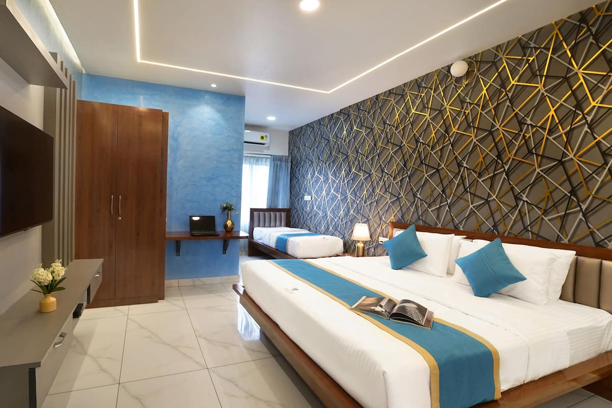 A modern hotel room with a large bed, a desk with a laptop, a TV, and a decorative wall.