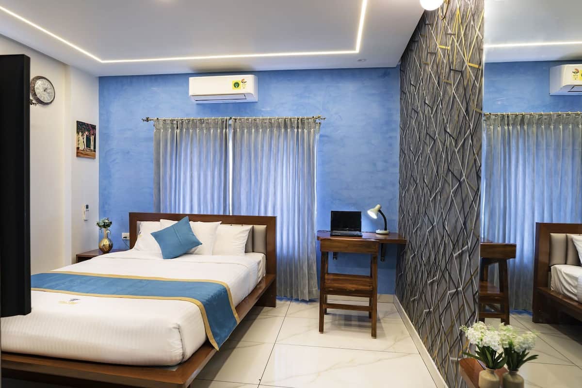 A hotel room with a bed, a desk, a laptop, a clock, and an air conditioner.