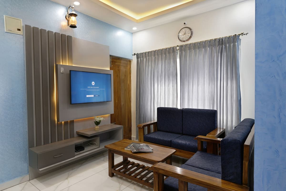 A modern living room with a flat-screen TV mounted on the wall, a dark blue sofa, a wooden coffee table, and a grey entertainment unit.