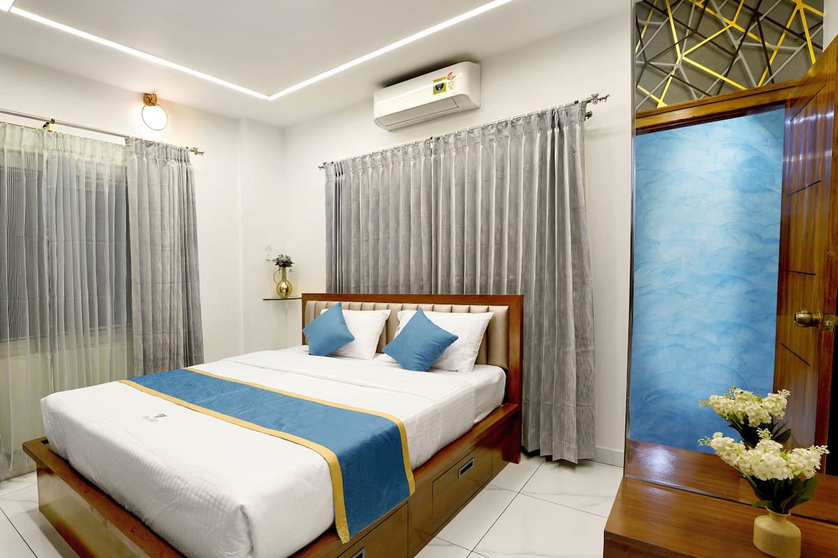 A bedroom with a bed, curtains, an air conditioning unit, a vase with flowers, and a wooden door.
