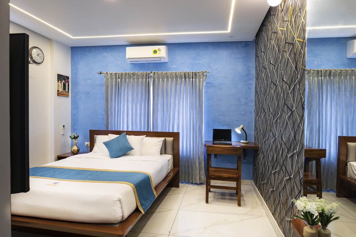 A hotel room with a bed, a desk, a laptop, and a nightstand.