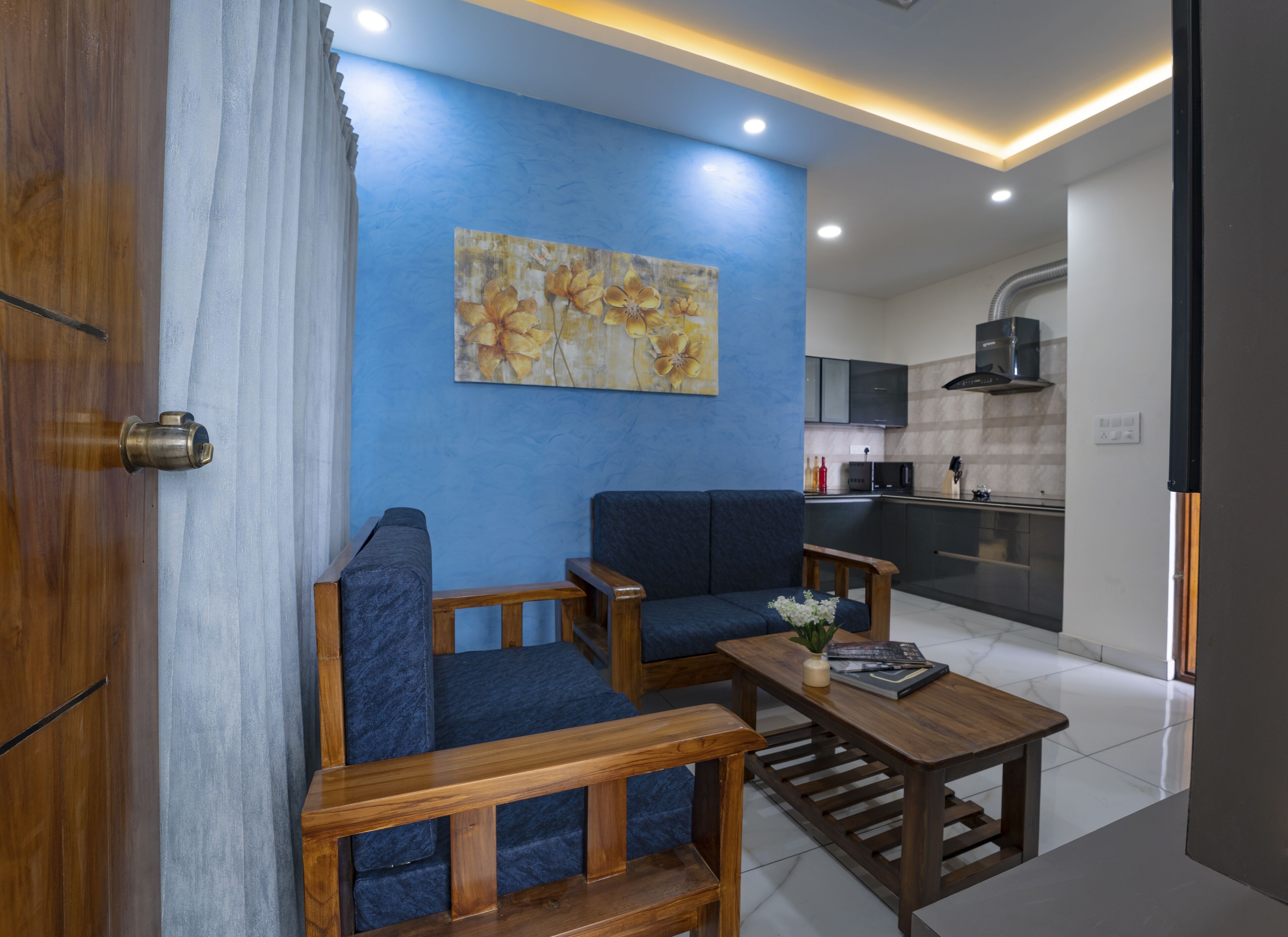 Ein modernes Wohnzimmer mit blauer Akzentwand, einer Couch, einem Couchtisch und einer Küche im Hintergrund.