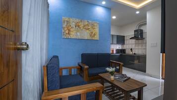 Ein modernes Wohnzimmer mit blauer Akzentwand, einer Couch, einem Couchtisch und einer Küche im Hintergrund.