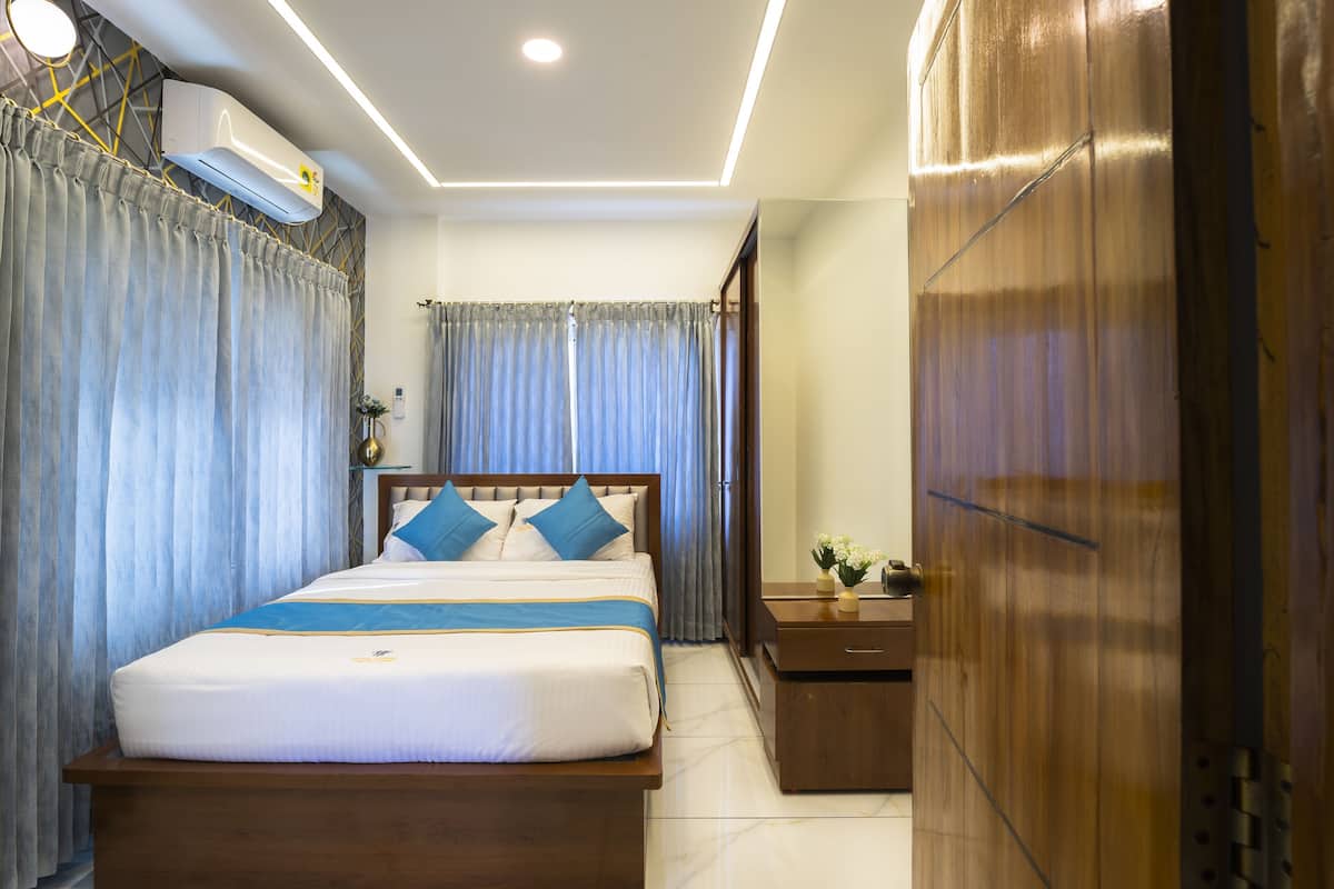 A hotel room with a bed, curtains, a bedside table, a mirror, and a wardrobe.