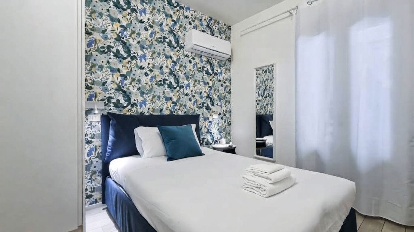 A hotel room with a bed, a nightstand, an air conditioning unit, and a bathroom visible through a door.