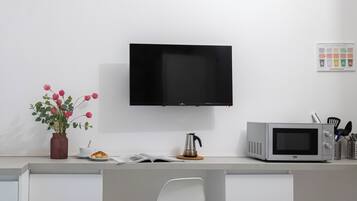 Eine Küche mit Flachbildfernseher, Mikrowelle, Kaffeemaschine, einer Blumenvase und einem Croissant auf der Arbeitsplatte.