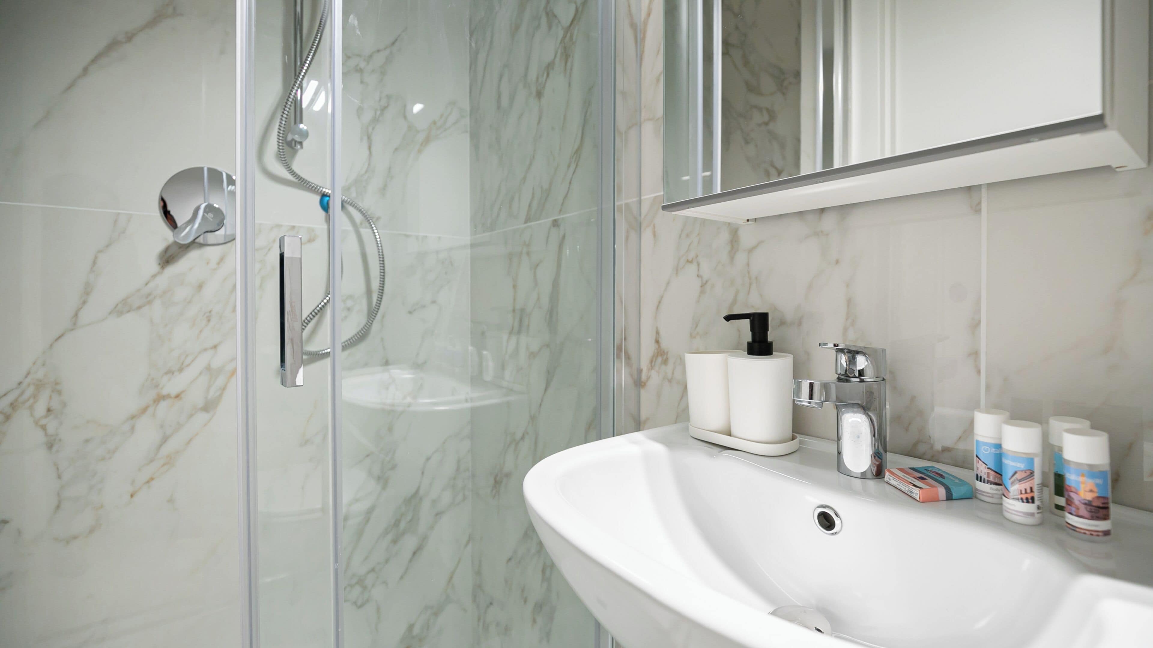 A bathroom with a glass shower enclosure, a white sink, and toiletries.