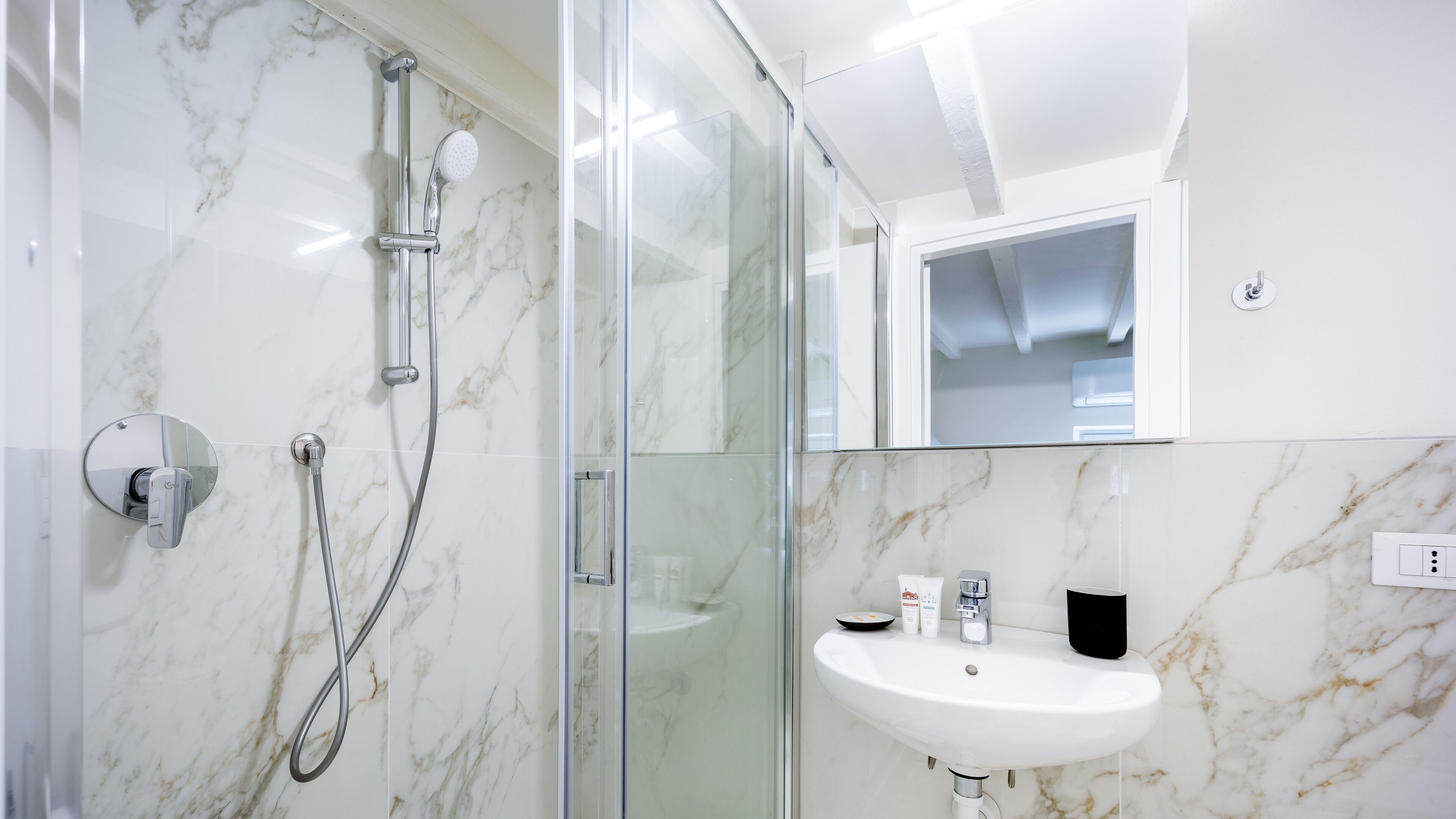 A modern bathroom with a glass shower enclosure, a white sink, and a mirror above the sink.