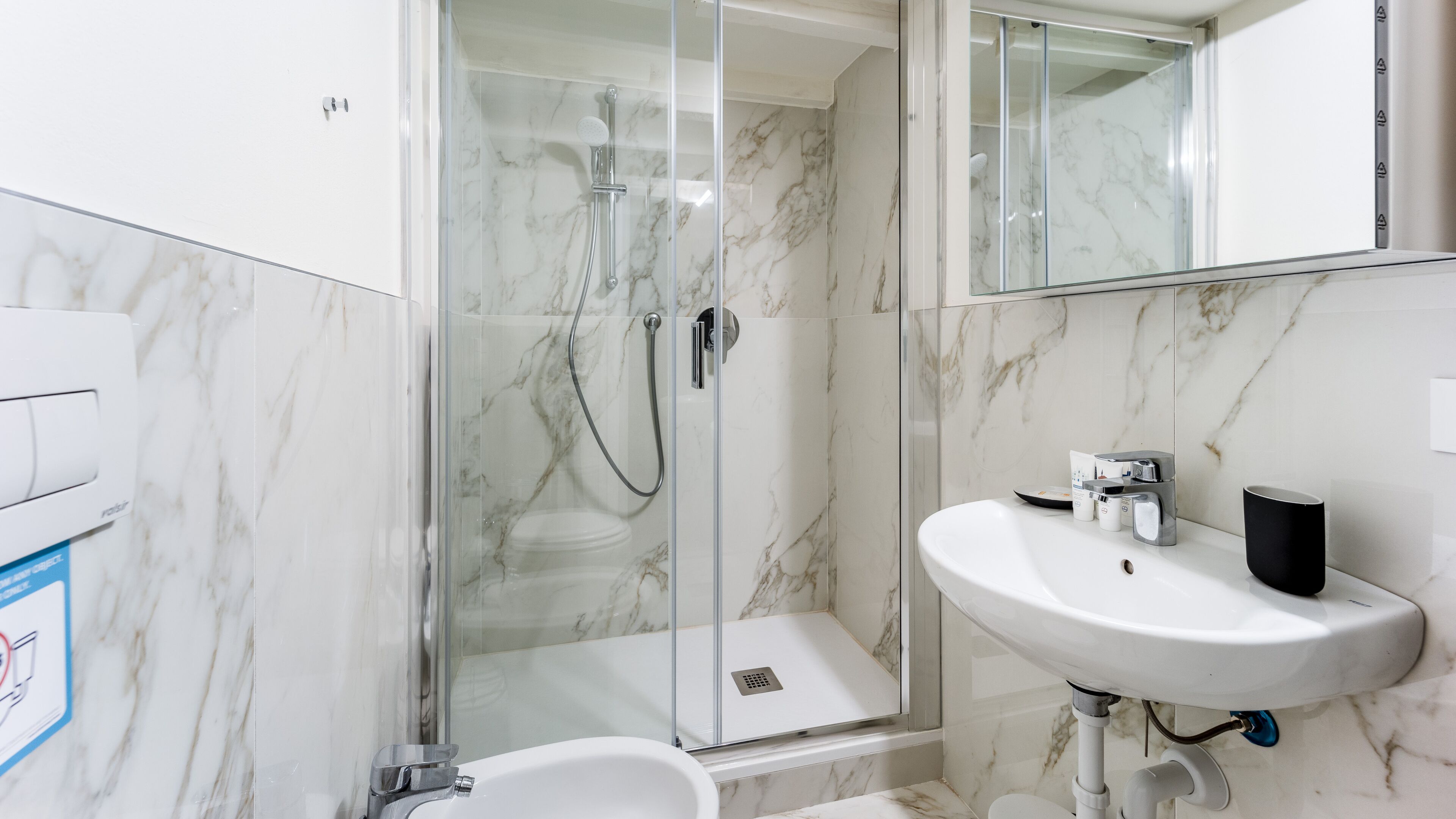 A modern bathroom with a glass-enclosed shower, a white sink, and marble walls.