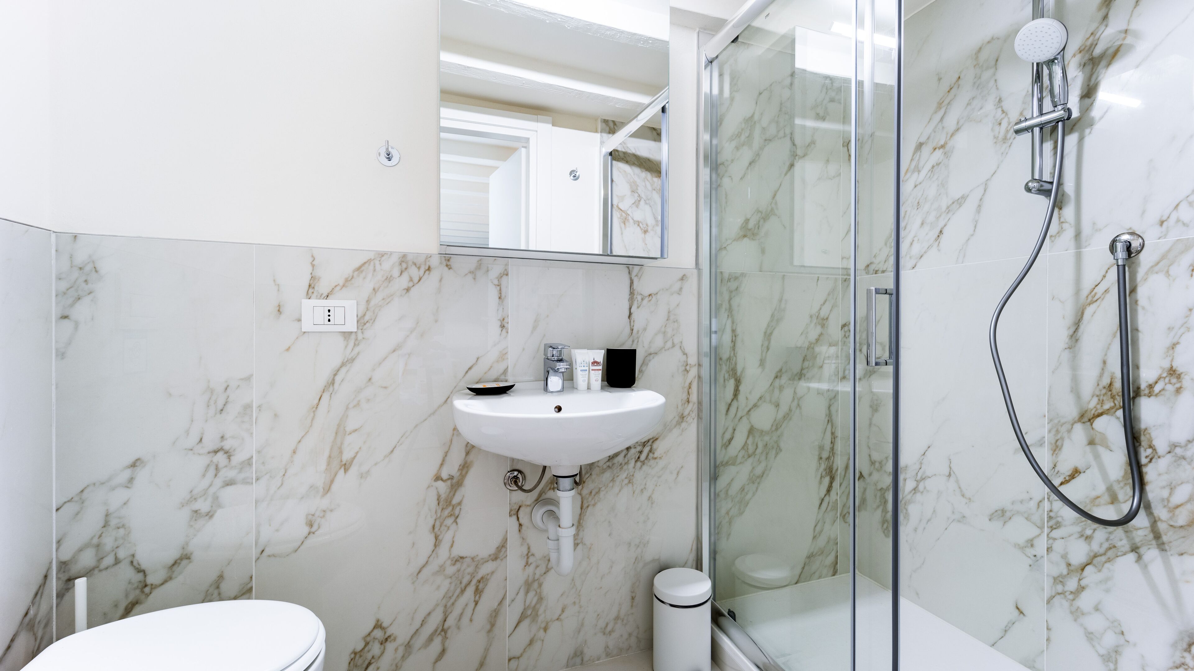 A modern bathroom with a marble backsplash, a white sink, and a glass-enclosed shower.